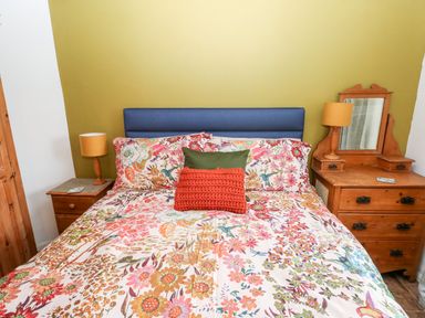 A bedroom with a bed floral bedding two bedside tables with lamps and a dresser with a mirror at The Coach House in St Florence