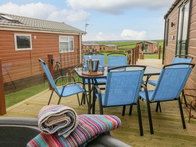 An outdoor deck with a table and six blue chairs a metal bucket on the table and rolled towels in the foreground at Oyster Lodge Broad Haven
