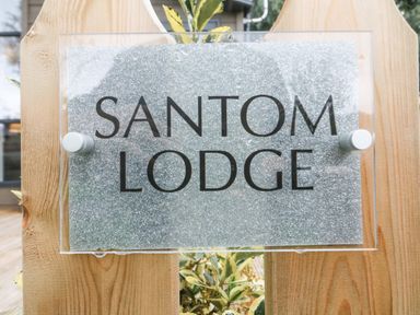 A sign with the text santom lodge on a wooden surface with plants behind it at Coniston View 9 Dock Acres near Tewitfield
