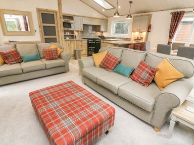 A living room with sofas cushions and a plaid ottoman next to a kitchen at Coniston View 9 in Dock Acres near Tewitfield