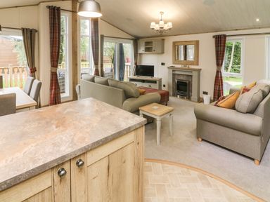 A living room with sofas a fireplace a TV and dining table visible at Coniston View 9 Dock Acres near Tewitfield