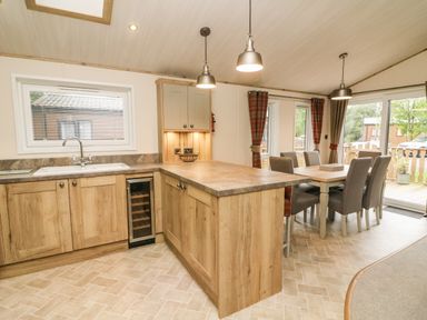 A kitchen with wooden cabinets and a dining area with chairs at Coniston View 9 Dock Acres near Tewitfield