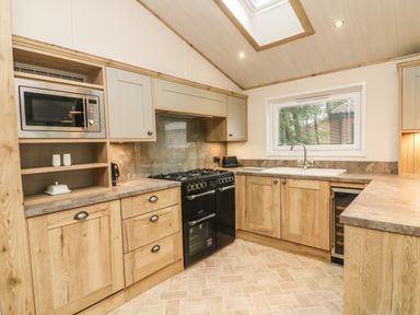 A kitchen with wooden cabinets a black stove a microwave sink and a window at Coniston View 9 Dock Acres near Tewitfield