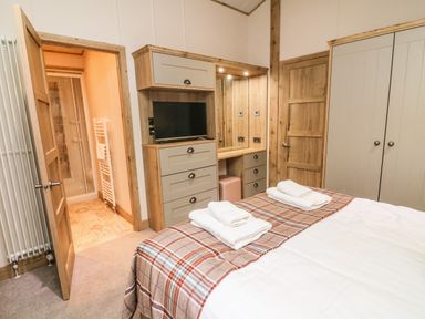 A bedroom with a bed and folded towels on a plaid runner a wardrobe and a door to a bathroom at Coniston View 9 Dock Acres near Tewitfield