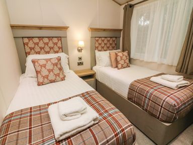 A bedroom with two single beds side by side with patterned cushions and plaid blankets at Coniston View 9 Dock Acres near Tewitfield