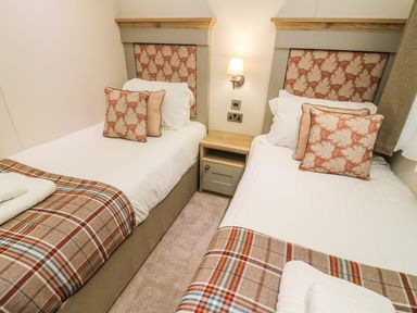 A bedroom with two single beds separated by a wooden nightstand with wall light at Coniston View 9 Dock Acres near Tewitfield