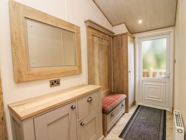 A hallway with a wooden cabinet mirror coat hooks bench and a door at Coniston View 9 Dock Acres near Tewitfield