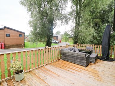 An outdoor wooden deck with a wicker sofa set and a potted plant at Coniston View 9 in Dock Acres near Tewitfield