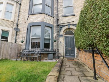 The exterior of a brick house with a gray door and bay windows a paved walkway and a green hedge at Westbourne House in Scarborough