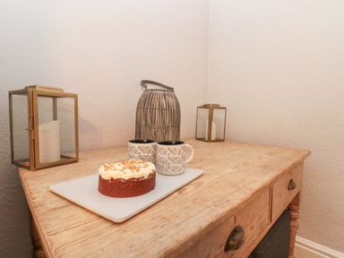 A wooden table with a cake on a cutting board two patterned mugs and three decorative candle holders at Westbourne House in Scarborough