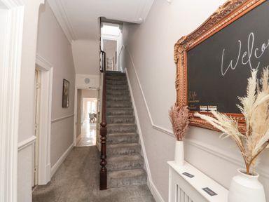 A hallway with carpeted stairs a blackboard with welcome message and dried plants in vases at Westbourne House in Scarborough