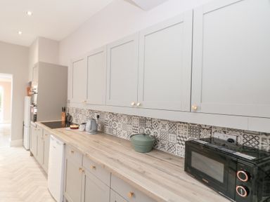 A kitchen with gray cabinets wooden countertop patterned tile backsplash microwave kettle and a pot at Westbourne House in Scarborough