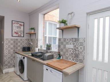 A kitchen with patterned tile backsplash a washing machine dishwasher and wooden countertop at Westbourne House in Scarborough