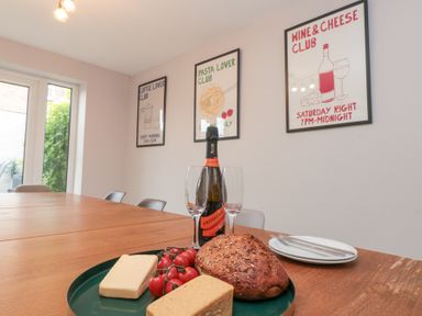 A dining table with bread cheese tomatoes a bottle of prosecco and two glasses in a room with posters on the wall at Westbourne House in Scarborough