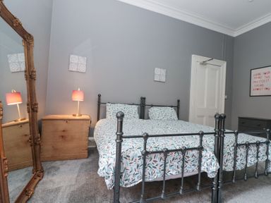 A bedroom with a black metal bed frame a wooden chest of drawers a large ornate mirror and grey walls at Westbourne House in Scarborough