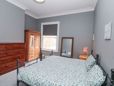A bedroom with a double bed a nightstand with a lamp a wooden wardrobe a chest of drawers and a mirror on the floor at Westbourne House in Scarborough