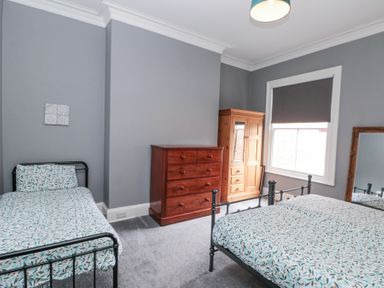 A bedroom with two iron beds a wooden chest of drawers a wooden wardrobe and a window with a blind at Westbourne House in Scarborough
