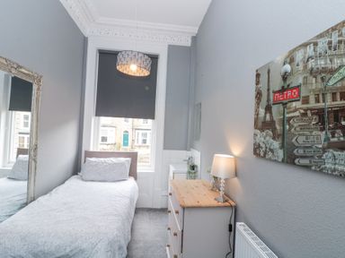 A small bedroom with a single bed a chest of drawers a lamp a large mirror and a paris wall art at Westbourne House in Scarborough