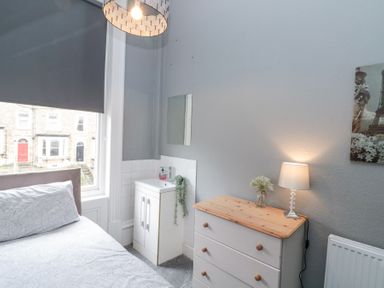 A bedroom corner with a bed next to a window a white dresser with a lamp and flowers and a small sink cabinet with a mirror above at Westbourne House in Scarborough