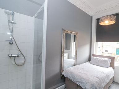 A bedroom with a bed next to a window and a shower enclosure beside a wall mirror at Westbourne House in Scarborough