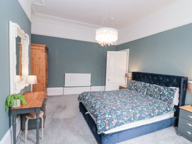 A bedroom with a bed a wooden wardrobe a small table with a lamp and plant and a wall mirror at Westbourne House in Scarborough