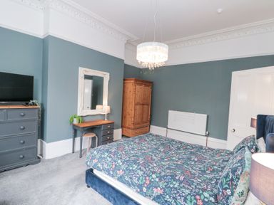 A bedroom with a large bed, a wooden wardrobe, a desk with a mirror above it, and a chest of drawers at Westbourne House Scarborough