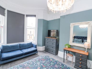 A bedroom with a blue sofa near windows a chest of drawers with a television a desk with a mirror and a lamp at Westbourne House in Scarborough