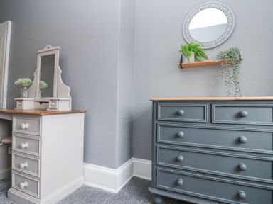 A room corner with a white dressing table with mirror and a gray chest of drawers with a shelf above holding plants at Westbourne House in Scarborough