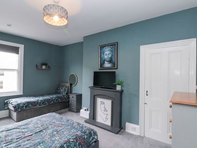 A bedroom with two beds a TV on a fireplace and paintings on the wall at Westbourne House in Scarborough