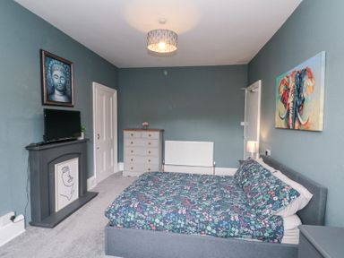 A bedroom with a bed with floral bedding a dresser a television on a mantel and artwork on walls at Westbourne House in Scarborough