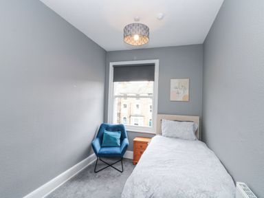 A small bedroom with a single bed next to a wooden nightstand and a blue chair near a window at Westbourne House in Scarborough