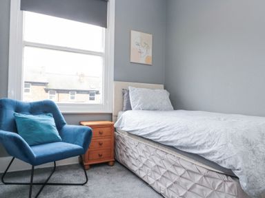 A bedroom with a single bed next to a wooden bedside table and a blue armchair by a window at Westbourne House in Scarborough