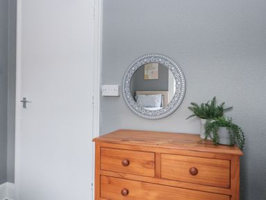 A wooden dresser with potted plants and a round mirror above it reflecting a bed at Westbourne House in Scarborough