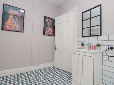 A bathroom with patterned floor tiles a white door a white sink cabinet and animal wall art at Westbourne House in Scarborough