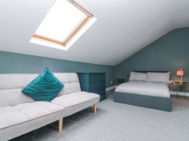A bedroom with a bed, sofa with a cushion, skylight window and bedside lamp at Westbourne House in Scarborough