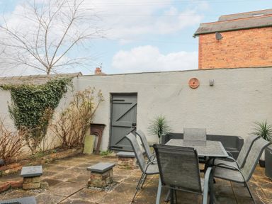 A patio with a table, six chairs, plants, and a gray door on a white wall at Westbourne House in Scarborough