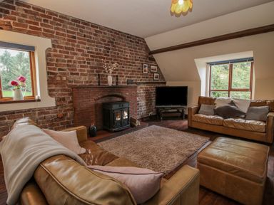 A living room with leather sofas a brick wall with a fireplace and windows at Owlbury Hall Barn in Snead near Bishops Castle Montgomery