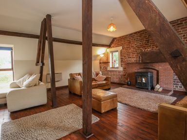 A living room with wooden beams leather sofas a fireplace and rugs at Owlbury Hall Barn in Snead near Bishops Castle Montgomery