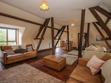 A living room with wooden beams brown leather sofas beige rugs and a dining table at Owlbury Hall Barn in Snead near Bishops Castle Montgomery