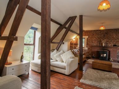 A living room with wooden beams a beige sofa a brick fireplace and wooden floors at Owlbury Hall Barn in Snead near Bishops Castle Montgomery