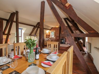 A dining table set with plates glasses and a vase of flowers in a room with exposed wooden beams and a fireplace at Owlbury Hall Barn Snead near Bishops Castle Montgomery