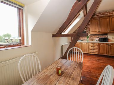 A kitchen with wooden table and white chairs under a sloped ceiling with exposed wooden beams at Owlbury Hall Barn Snead near Bishop's Castle Montgomery