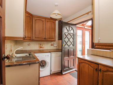 A kitchen with wooden cabinets a washing machine a dishwasher a sink a door with glass panels and tiled floor at Owlbury Hall Barn in Snead near Bishops Castle Montgomery