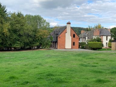 A grass lawn with a group of houses and trees in the background at Owlbury Hall Barn in Snead near Bishops Castle Montgomery