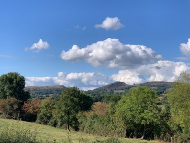 A landscape with green trees and hills under a blue sky with clouds at Owlbury Hall Barn Snead near Bishops Castle Montgomery