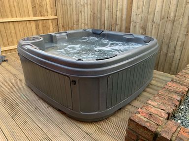 A hot tub on a wooden deck next to a brick wall and a wooden fence at Owlbury Hall Barn in Snead near Bishop's Castle Montgomery