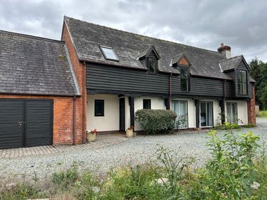 A two story house with a gravel driveway and plants in front at Owlbury Hall Barn Snead near Bishops Castle Montgomery