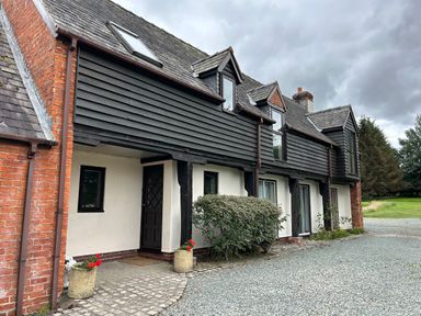 Exterior of a traditional house with black wooden cladding and white walls with gravel driveway at Owlbury Hall Barn in Snead near Bishop's Castle Montgomery