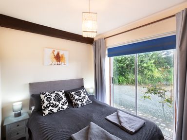A bedroom with a double bed with patterned pillows bedside tables lamps and a sliding glass door at Owlbury Hall Barn in Snead near Bishops Castle Montgomery