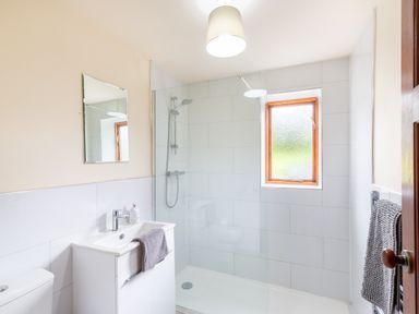 A bathroom with a shower area a white sink and cabinet a wall mirror a window and towels at Owlbury Hall Barn in Snead near Bishops Castle Montgomery